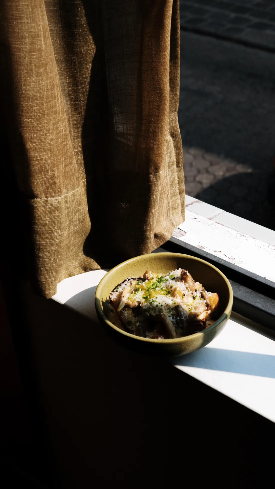 Platillo servido junto a una ventana, con luz de tarde y una cortina de lino
